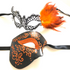 Black and orange couples masquerade mask set featuring men’s black mask with orange glitter scrolls and women’s filigree mask with orange feathers.