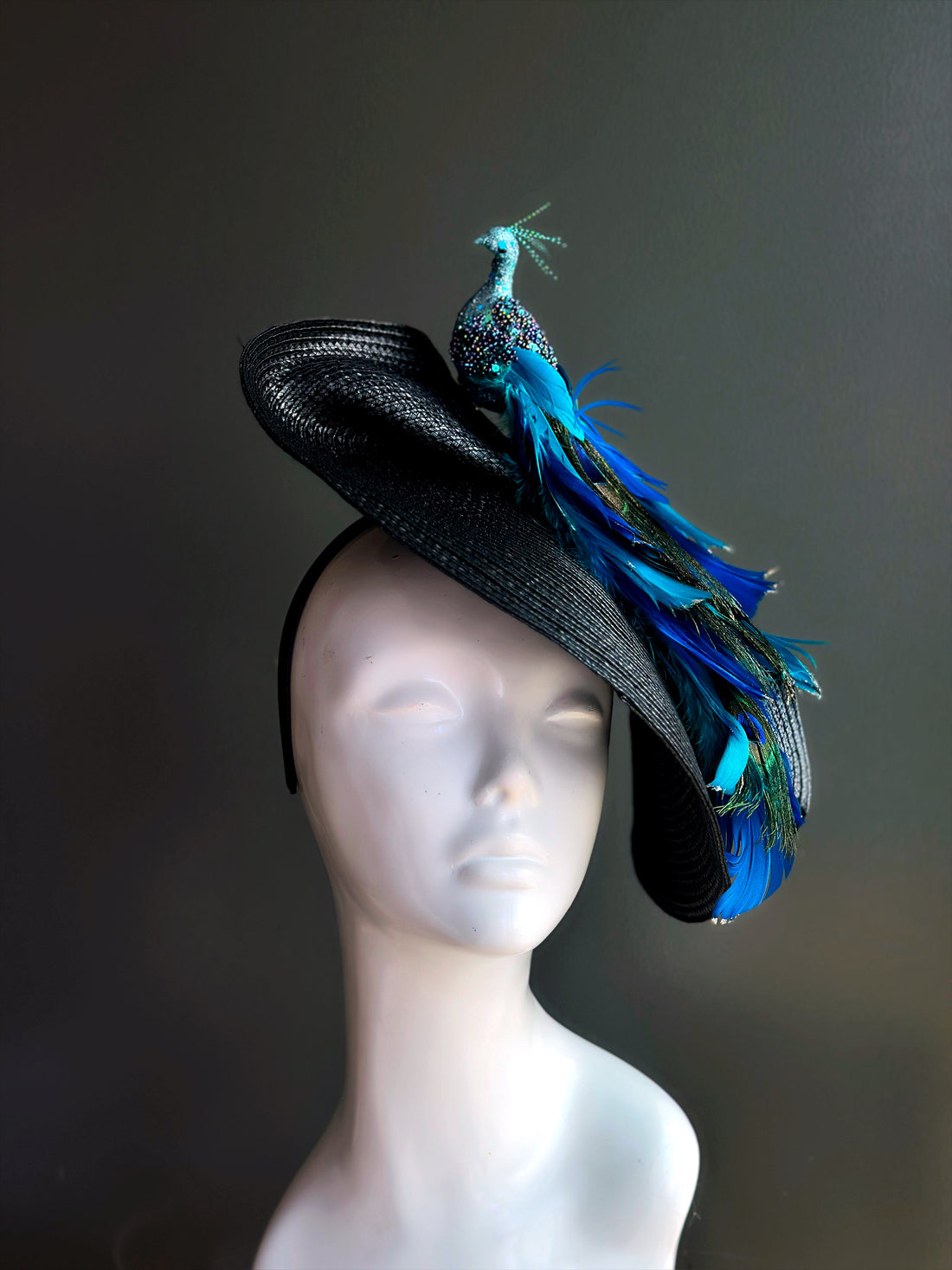 Tea party fascinator hat in black with jeweled peacock and cascading blue feathers.