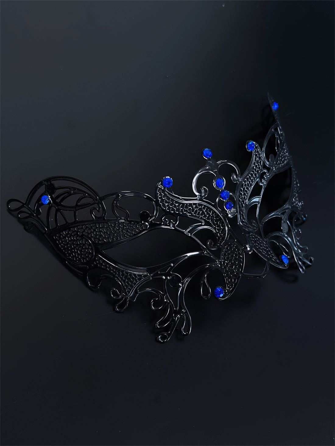 Black filigree masquerade mask with sapphire blue rhinestones, ideal for women attending Venetian masquerade balls, Mardi Gras, and Halloween parties.