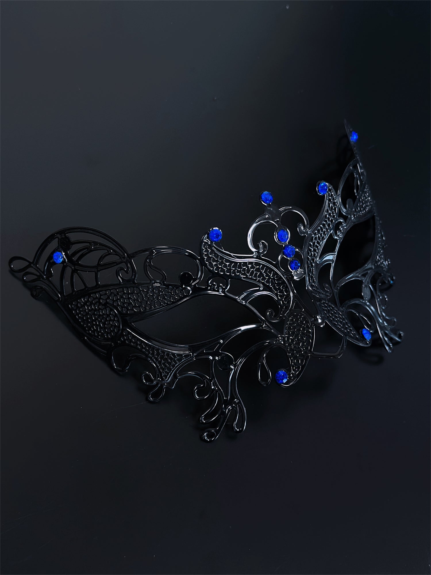 Black filigree masquerade mask with sapphire blue rhinestones, ideal for women attending Venetian masquerade balls, Mardi Gras, and Halloween parties.