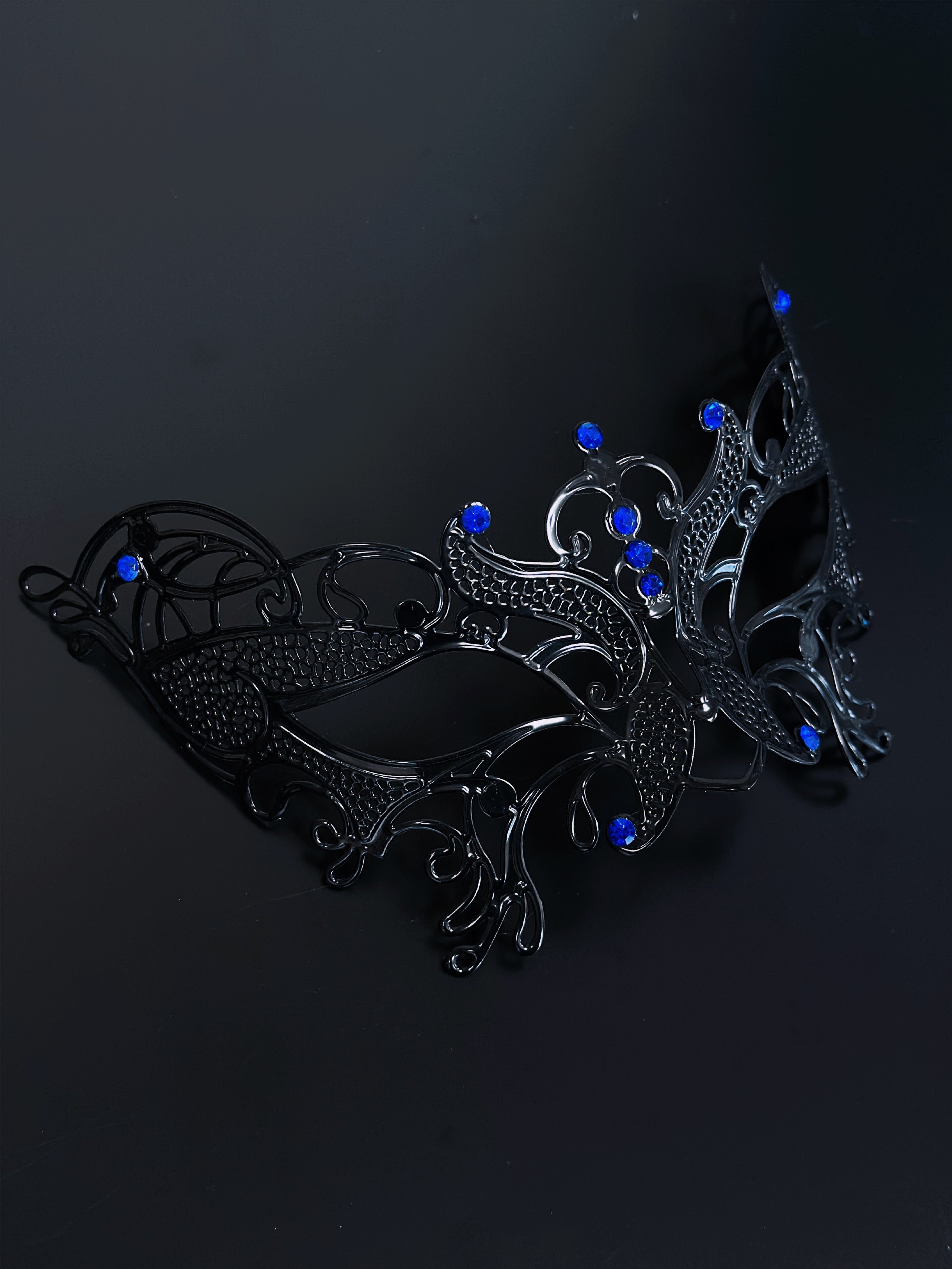 Black filigree masquerade mask with sapphire blue rhinestones, ideal for women attending Venetian masquerade balls, Mardi Gras, and Halloween parties.