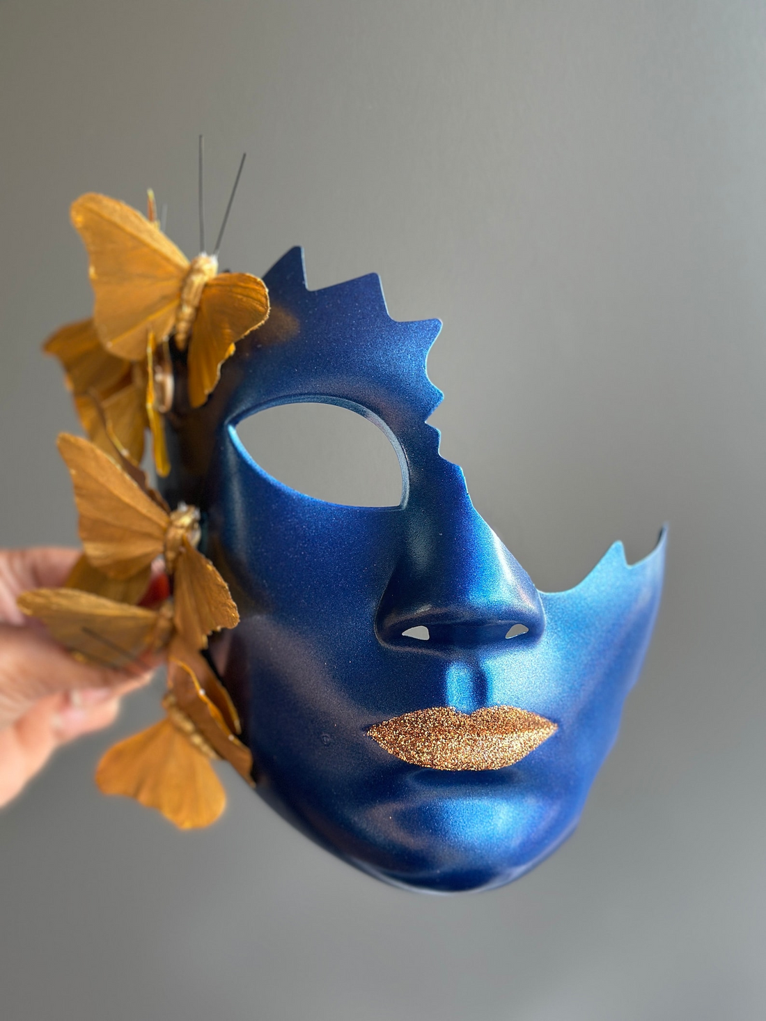 Avant-garde blue masquerade mask with golden butterflies and glitter lips.