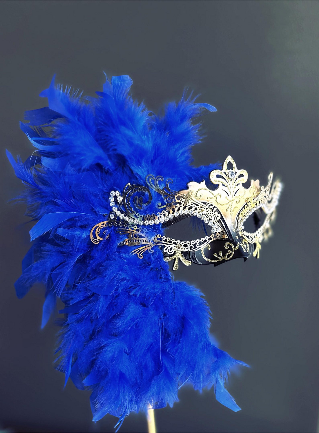 Venetian blue and gold feather masquerade mask on stick with glitter accents.