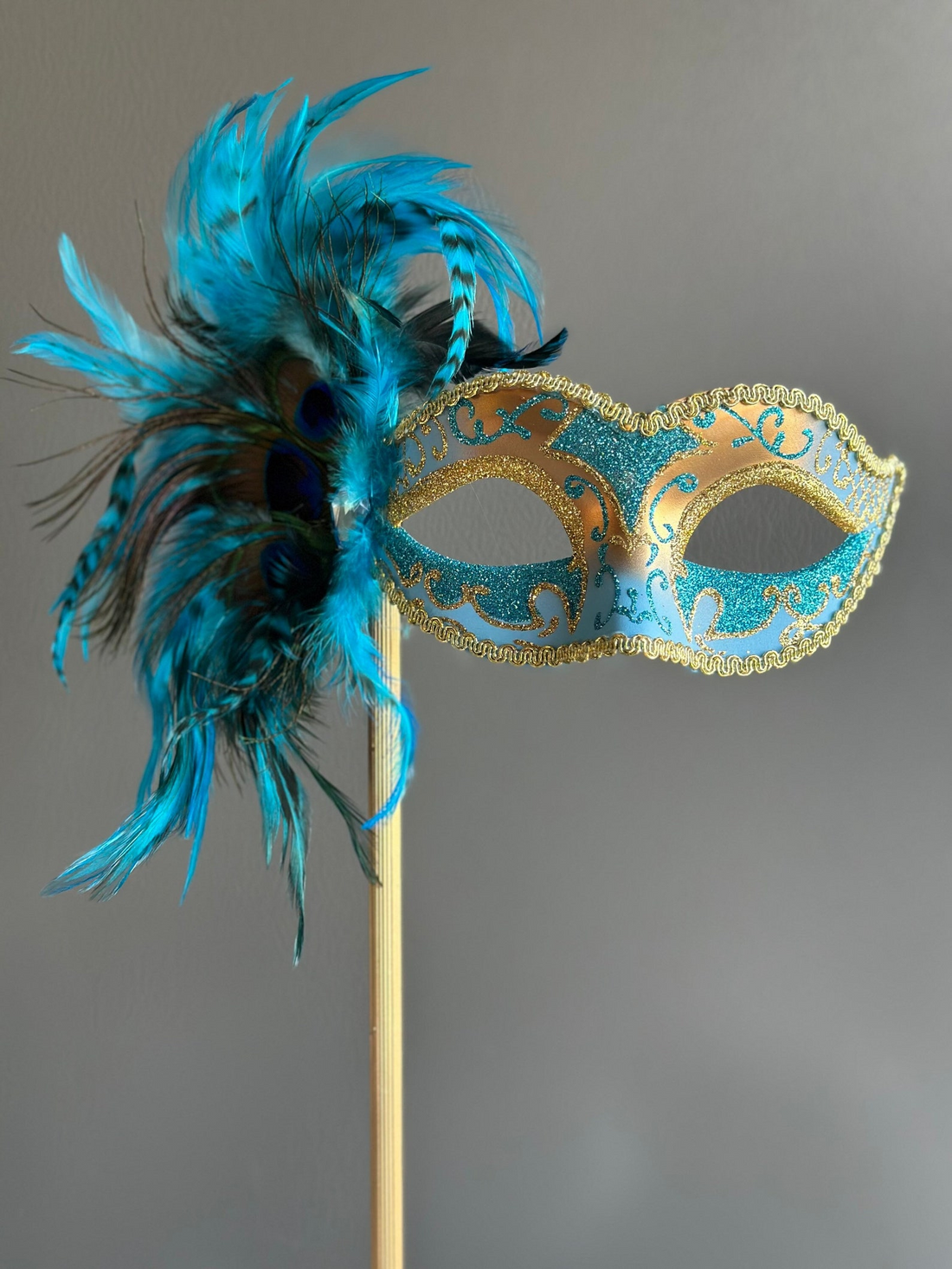 Venetian blue and gold feather masquerade mask on stick with glitter detailing.