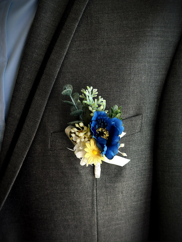 Bright groom boutonniere with navy blue flower, yellow daisy, and eucalyptus details for wedding or prom