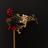 Gold filigree Christmas masquerade mask with holly berries, pinecone, and evergreen accents on a stick.