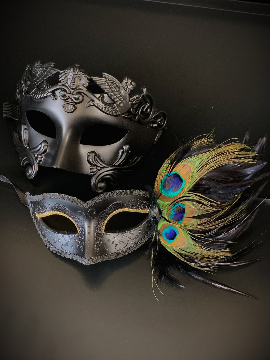 Couples mask set with a black gladiator mask for the man and a black peacock mask with gold glitter eyes.