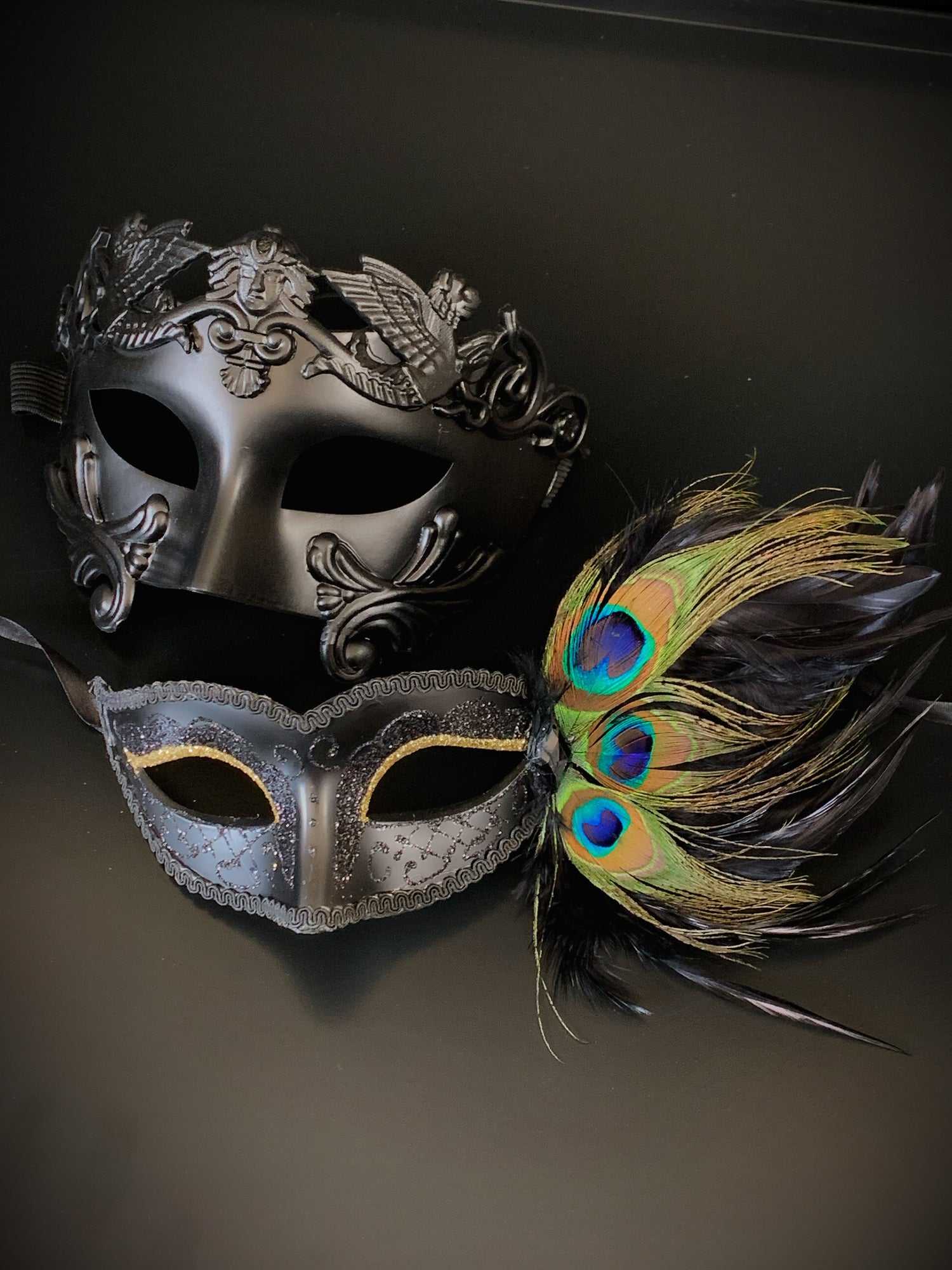 Couples mask set with a black gladiator mask for the man and a black peacock mask with gold glitter eyes.