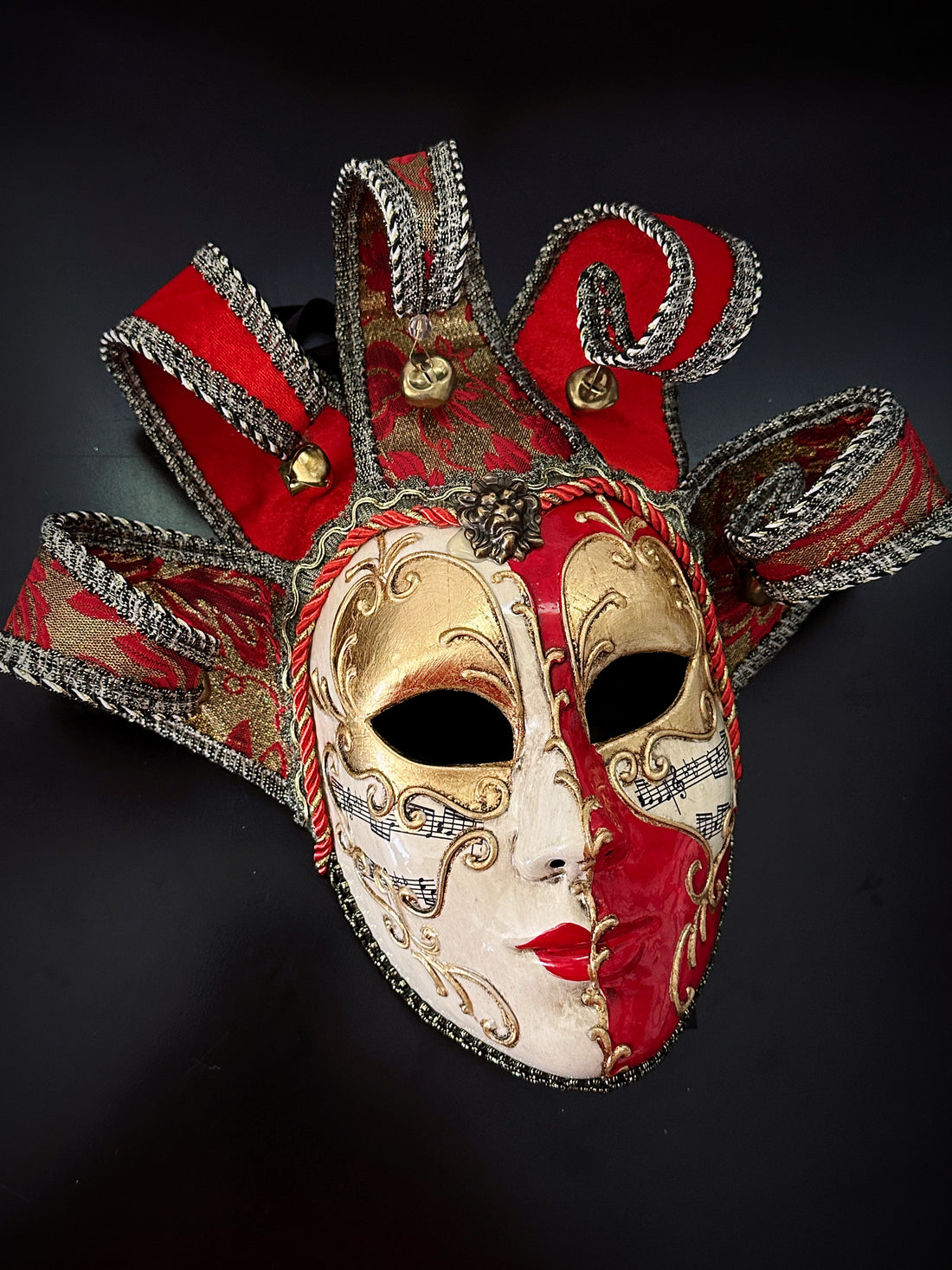 Venetian red and gold jester mask with baroque detailing and curled horns tipped with bells.