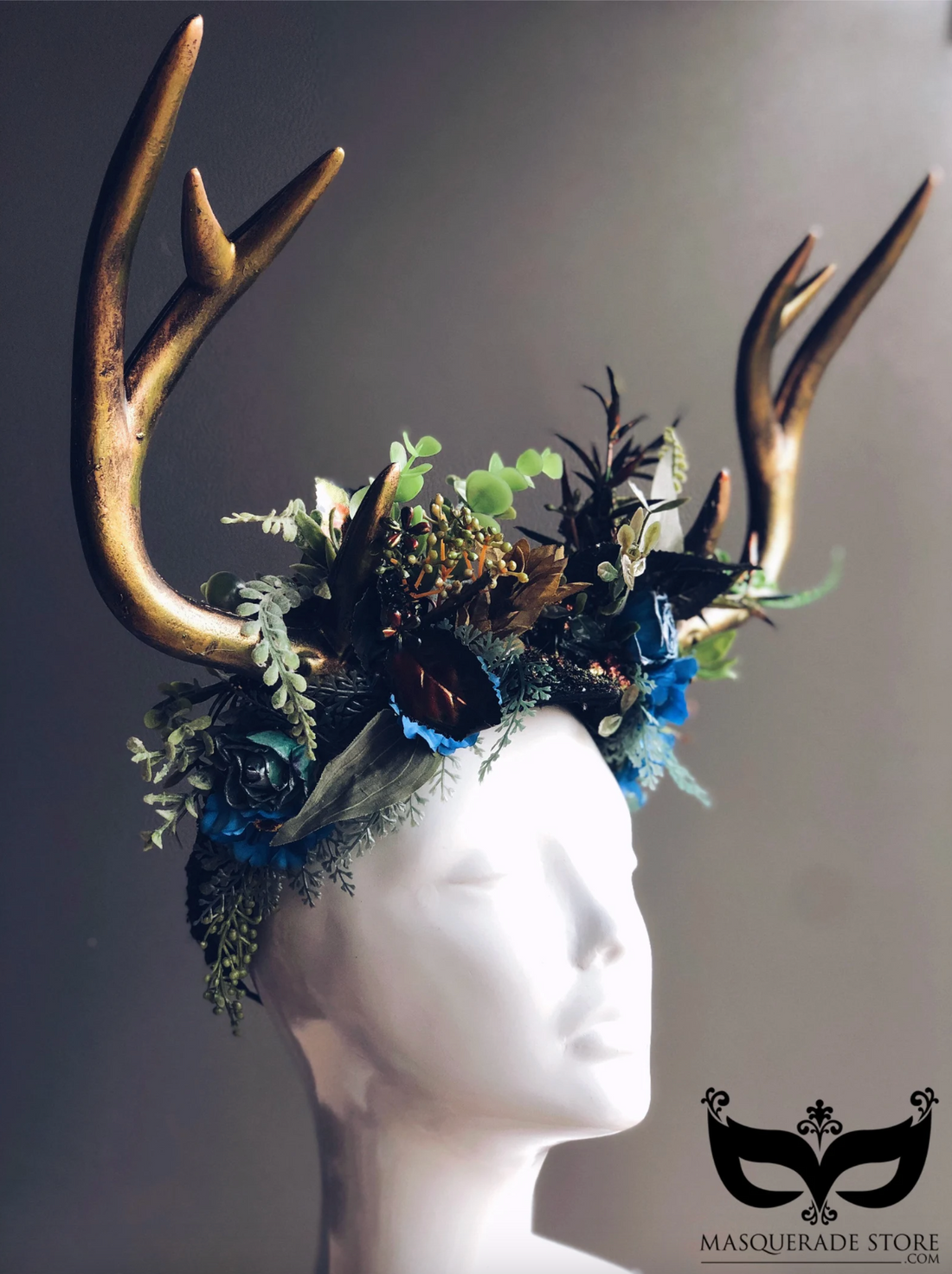 Gold deer antler masquerade crown decorated with green foliage and blue flowers for masquerade balls or fairy tale parties.