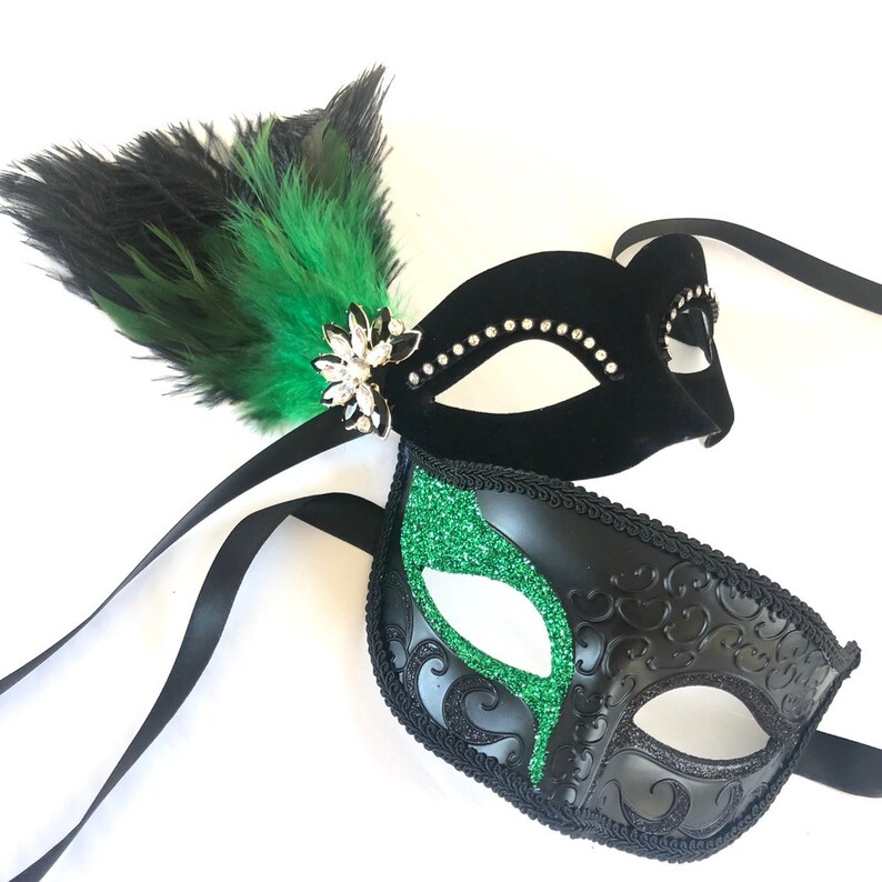 Couples masquerade mask set featuring a men’s black mask with emerald glitter and a women’s velvet mask with feathers and rhinestones.
