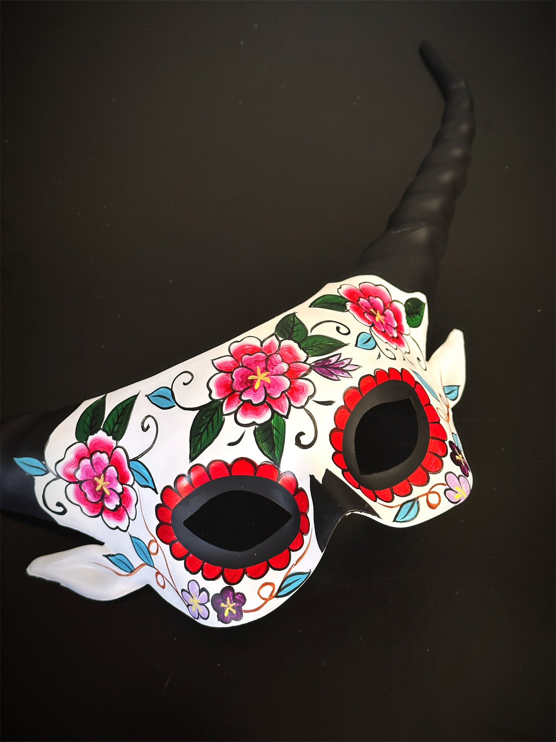 Painted masquerade skull mask with pink flowers and horns, perfect for Day of the Dead or fiesta events

