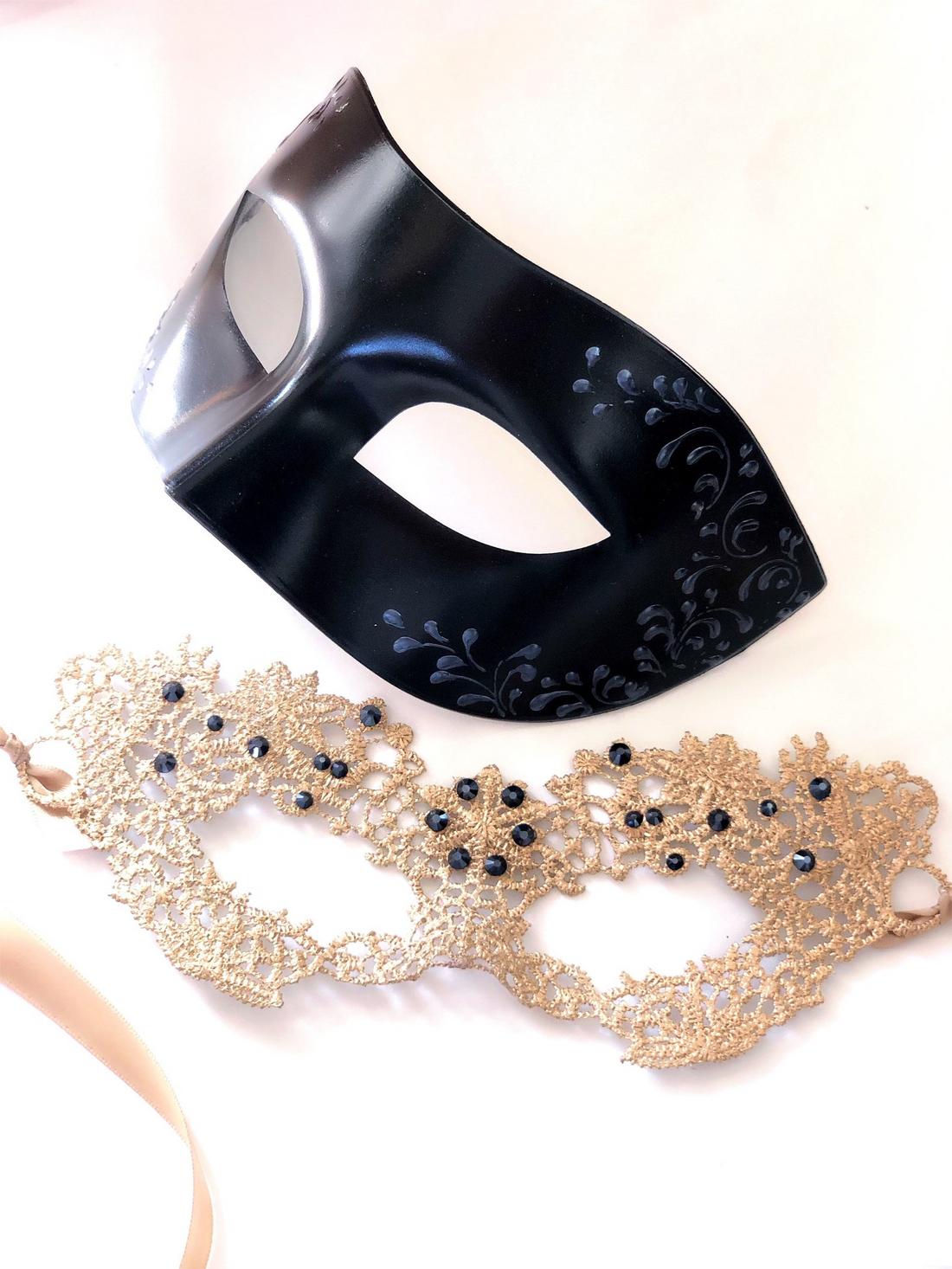 Couples masquerade mask set featuring black vegan leather men’s mask and gold lace women’s mask with gemstone accents.