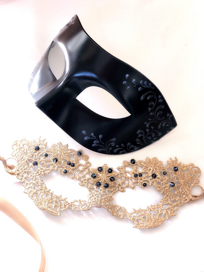 Couples masquerade mask set featuring black vegan leather men’s mask and gold lace women’s mask with gemstone accents.