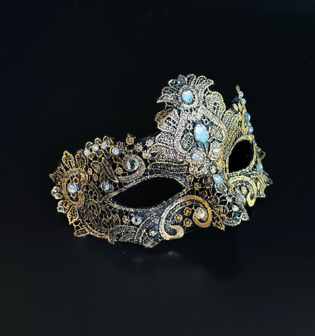 This black and gold masquerade mask features metallic embroidered lace with clear crystal accents, offering lightweight structure and balanced comfort for extended evening wear.