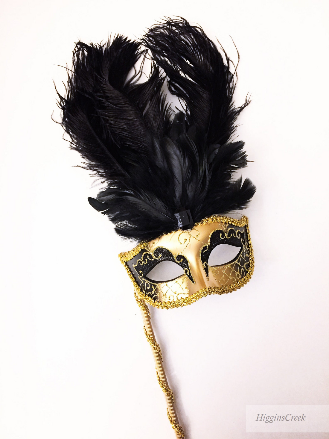 Venetian gold and black masquerade mask on stick with tall black ostrich feathers.