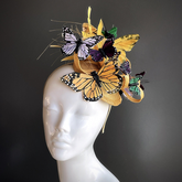 Gold Flutter Majesty Fascinator with butterflies in shades of gold, purple, and green, set atop an elegant gold base. 
