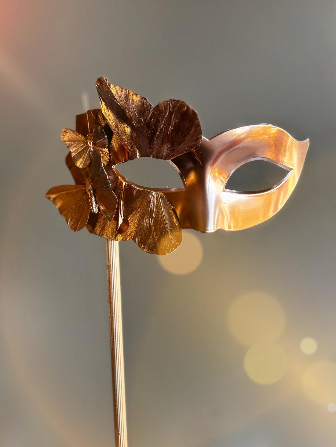 Gold Venetian masquerade mask on stick with butterfly and leaf accents.