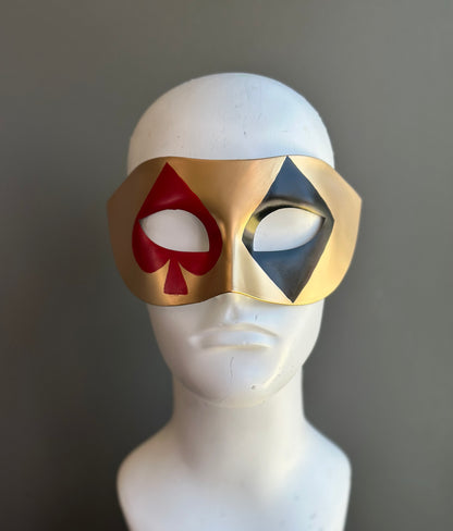 Gold casino masquerade mask with red and black playing card suit motifs on Venetian eye-mask silhouette
