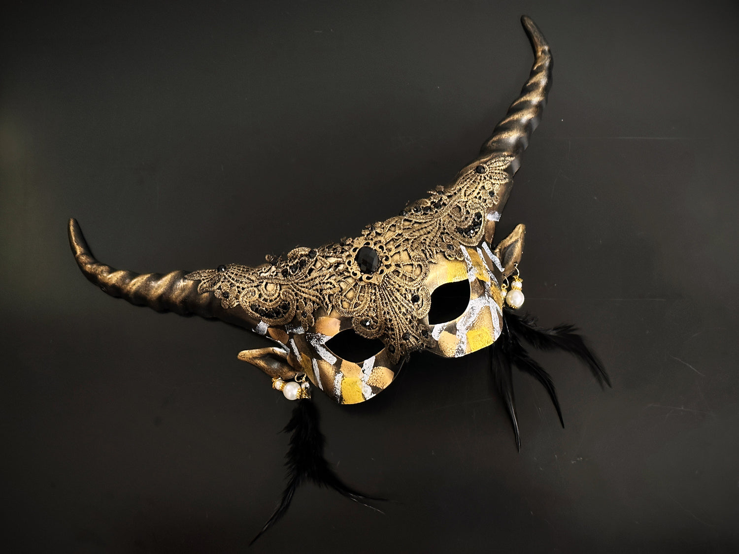 Black and gold horn masquerade mask with gothic lace, pearl earrings, and feathers – fantasy costume accessory.