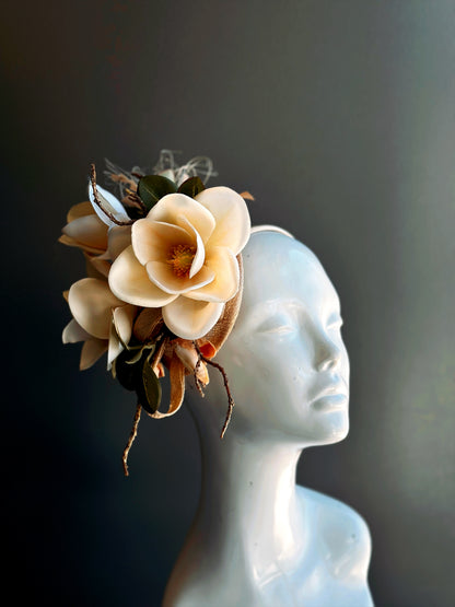 Elegant cream magnolia fascinator hat with gold leaf accents for weddings and tea parties.