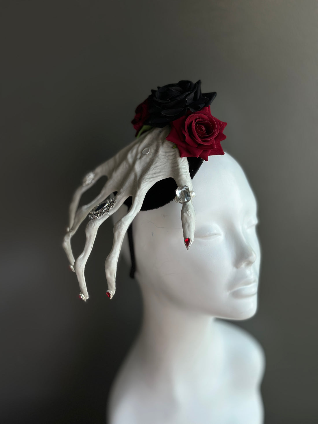 Halloween fascinator hat with skeletal hand and black red roses gothic headpiece.
