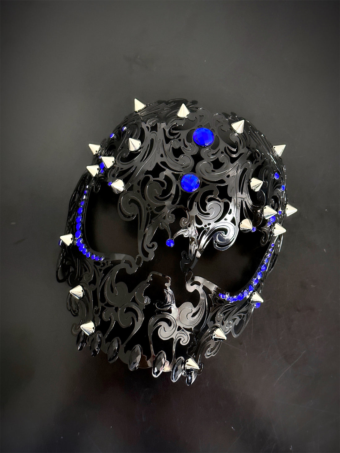Black skull masquerade mask with silver spikes and royal blue rhinestones