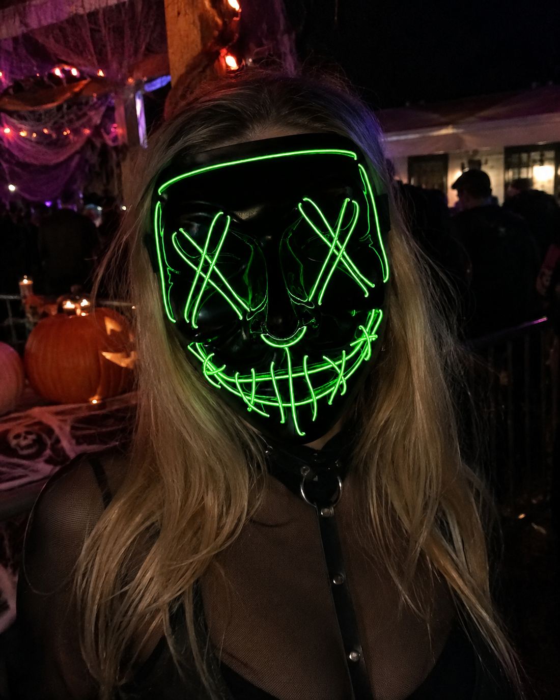 Green Voltage LED light-up mask with glowing green X eyes, stitched smile design, full-face shape, replaceable battery, and three lighting settings.