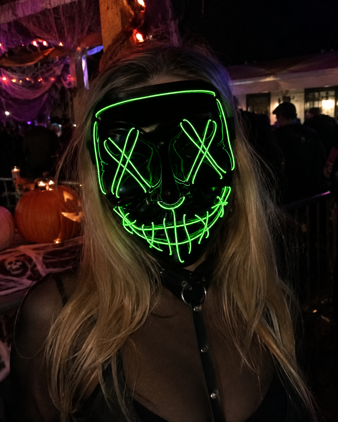 Green Voltage LED light-up mask with glowing green X eyes, stitched smile design, full-face shape, replaceable battery, and three lighting settings.