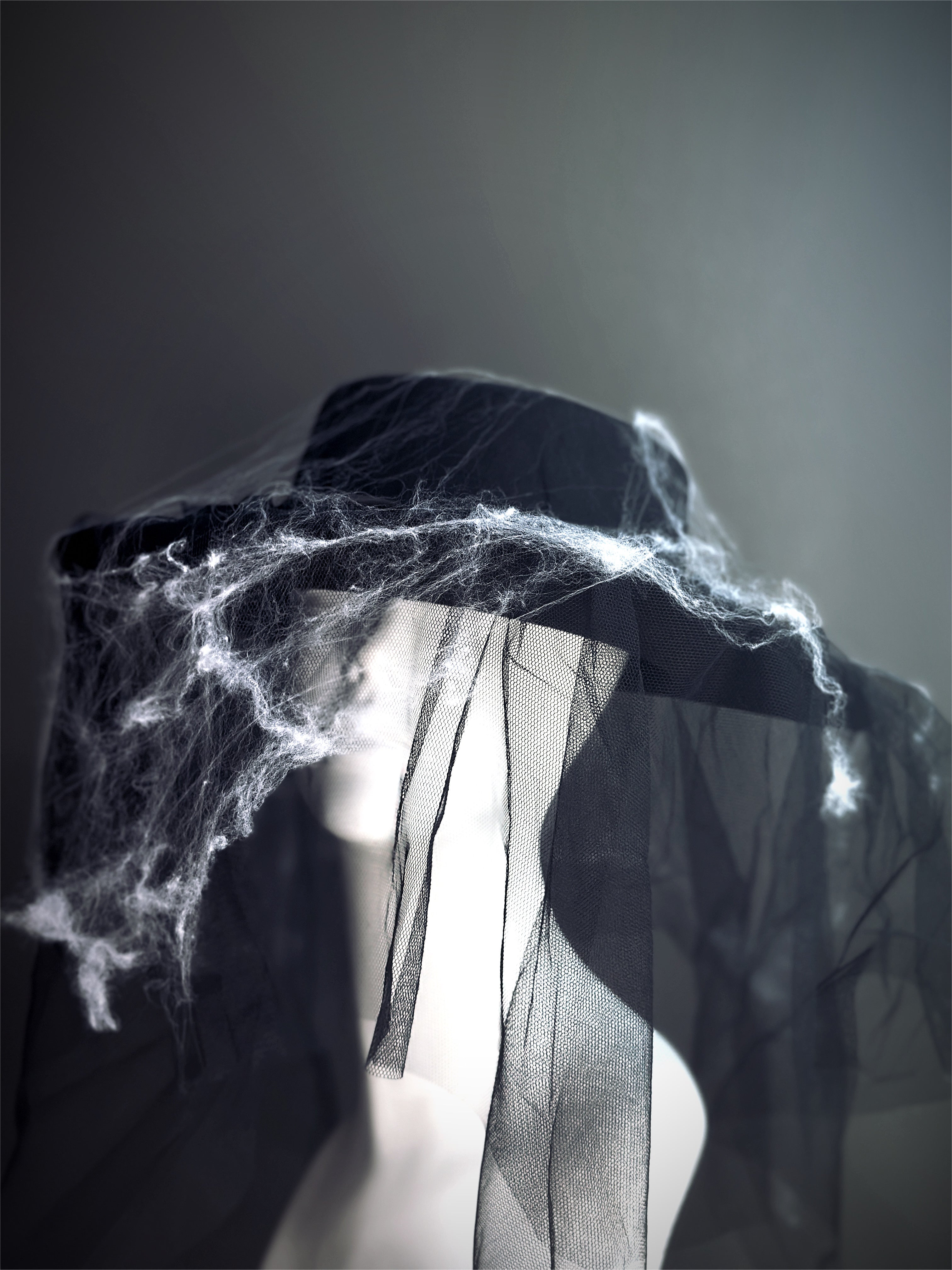 Halloween witch hat in black with mesh veil and cobweb accents, spooky gothic accessory.