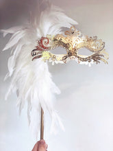 Handheld Venetian mask with white feathers, gold trim, and sparkling rhinestones.