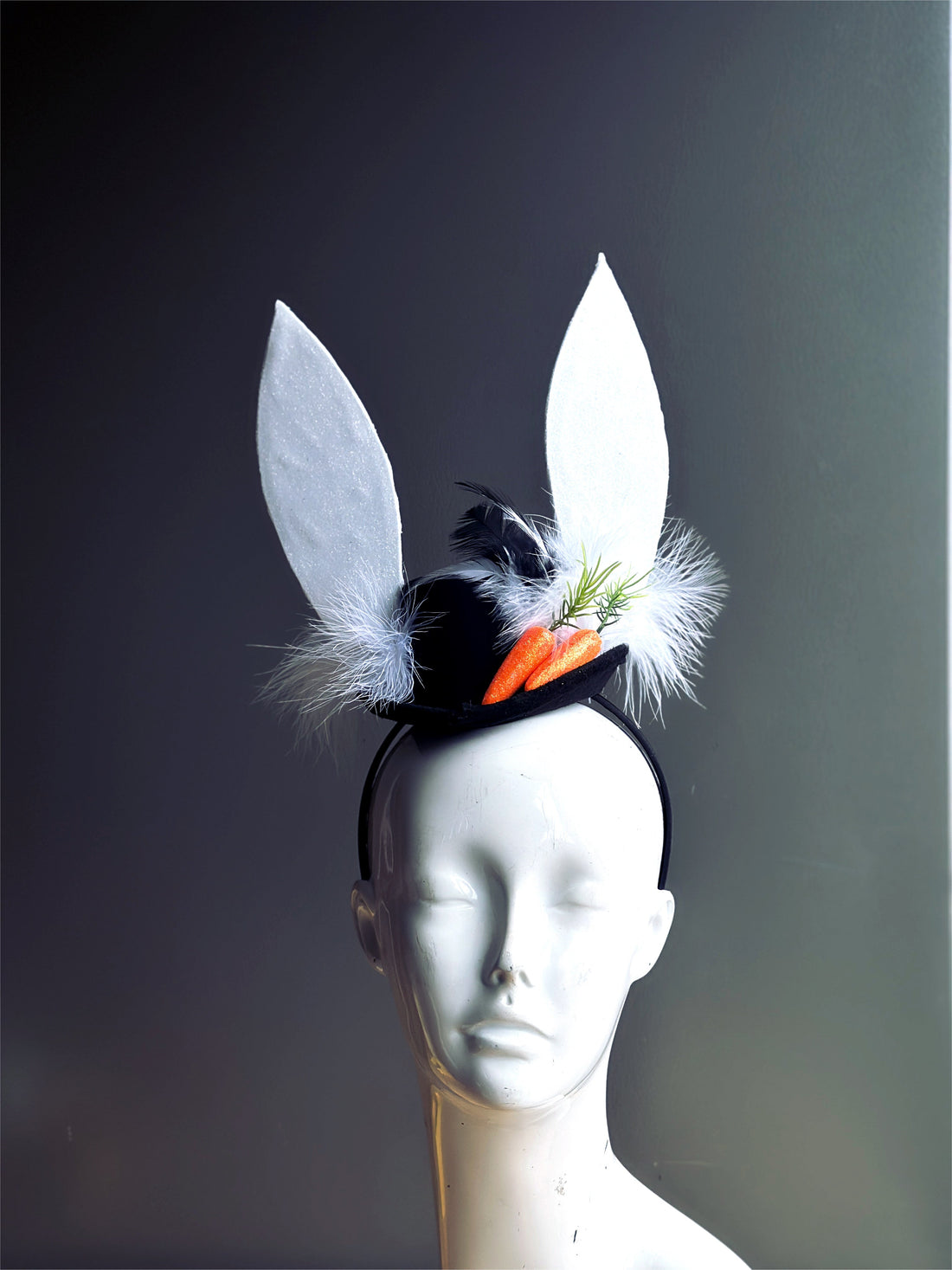 Black hat with white bunny ears, white feathers, and orange carrots.