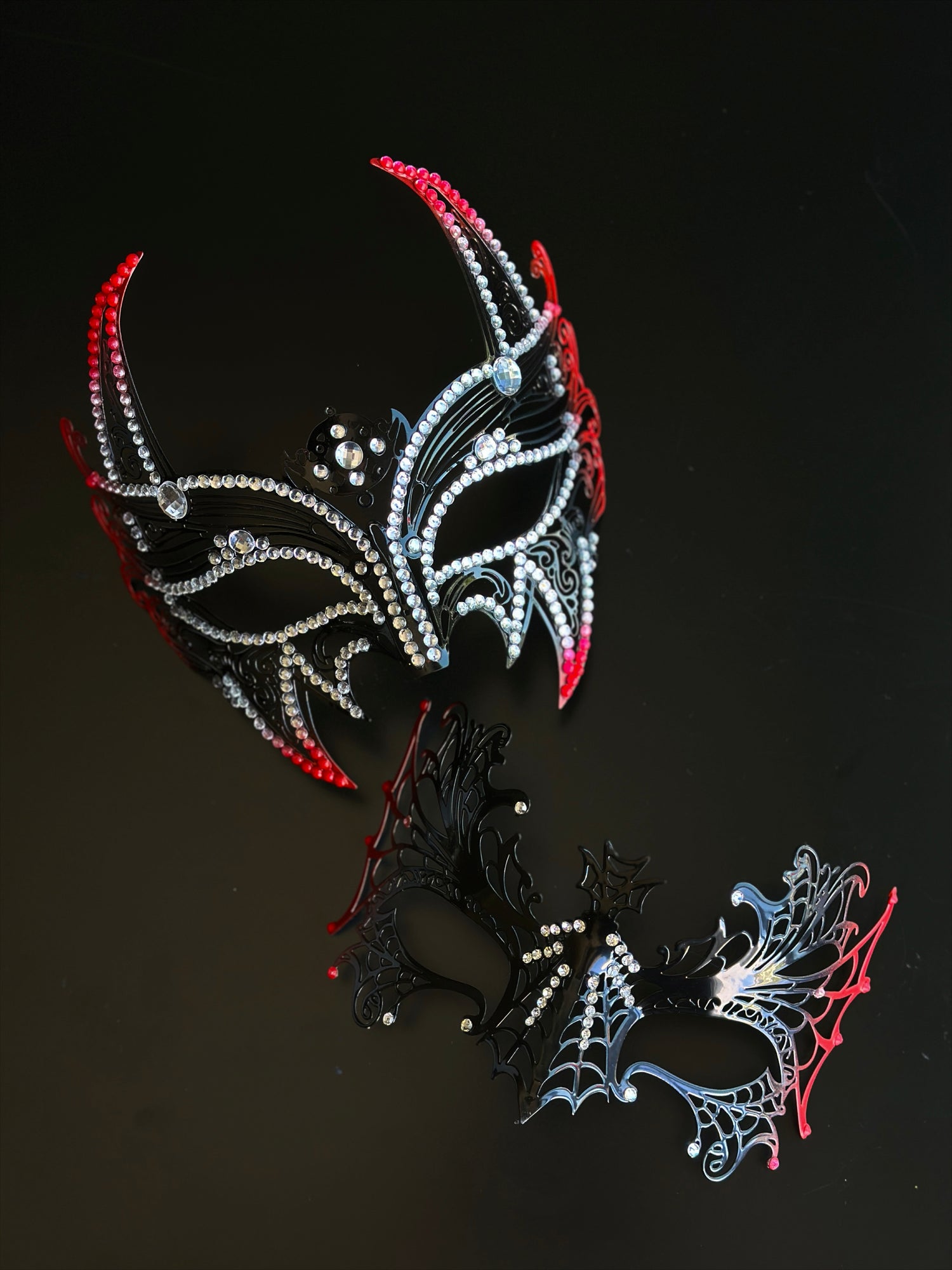 Red and black couples masquerade mask set with a horned rhinestone masquerade mask and a spiderweb-style eye mask for gothic formal events.