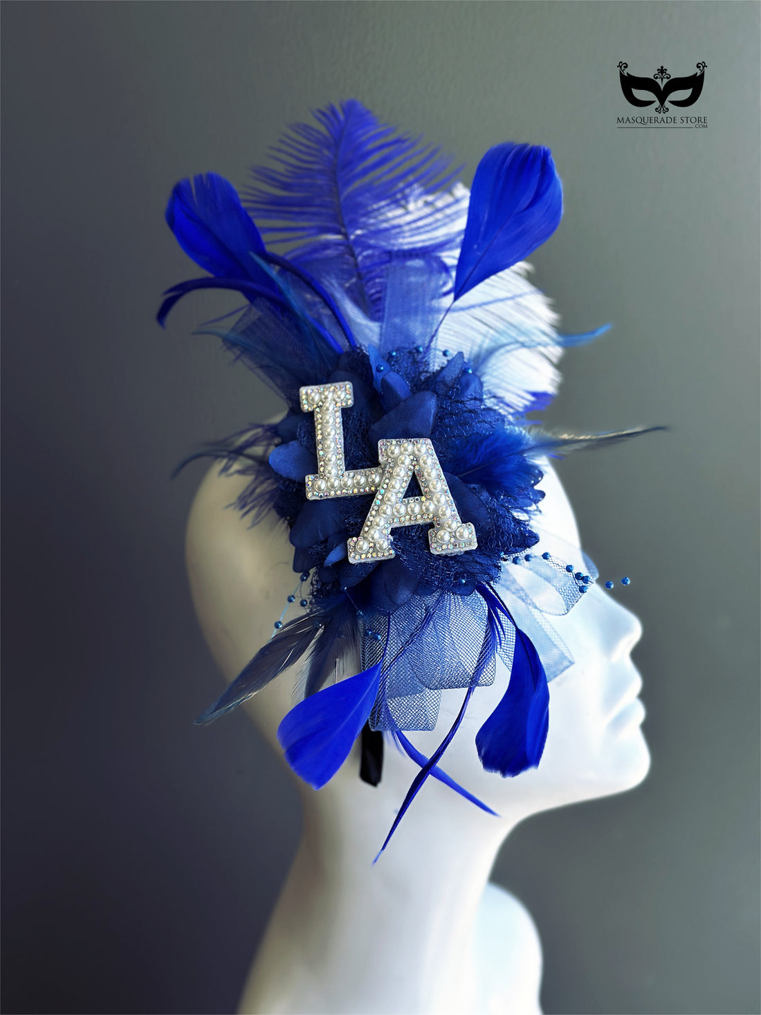 Royal blue LA fascinator with layered feathers, floral accents, blue tulle, pearl rhinestone letter details, and statement game-day styling.