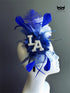 Royal blue LA fascinator with layered feathers, floral accents, blue tulle, pearl rhinestone letter details, and statement game-day styling.