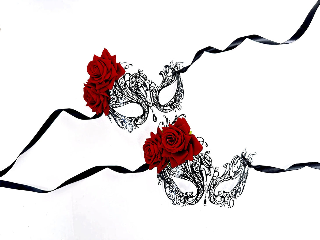 Set of two masquerade masks in black laser cut metal adorned with red roses and clear rhinestones.