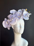 Lavender orchid fascinator hat with oversized floral bouquet headpiece.