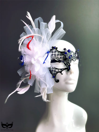 Patriotic masquerade mask with black filigree base, blue crystals, and dramatic red, white, and blue feather accents for women’s masquerade events.