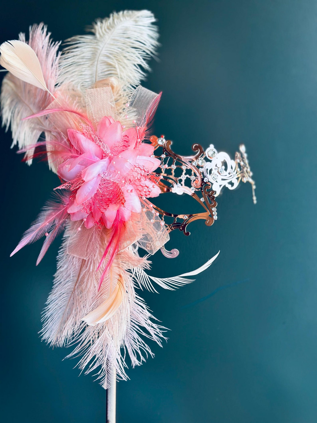 Rose gold masquerade mask with peach pink feathers and floral accent.