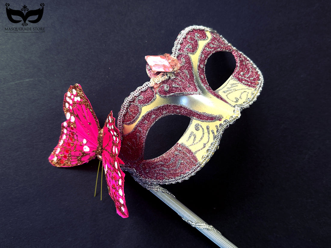Pink masquerade mask on a stick with glitter details, butterfly accent, and silver trim for prom and Mardi Gras
