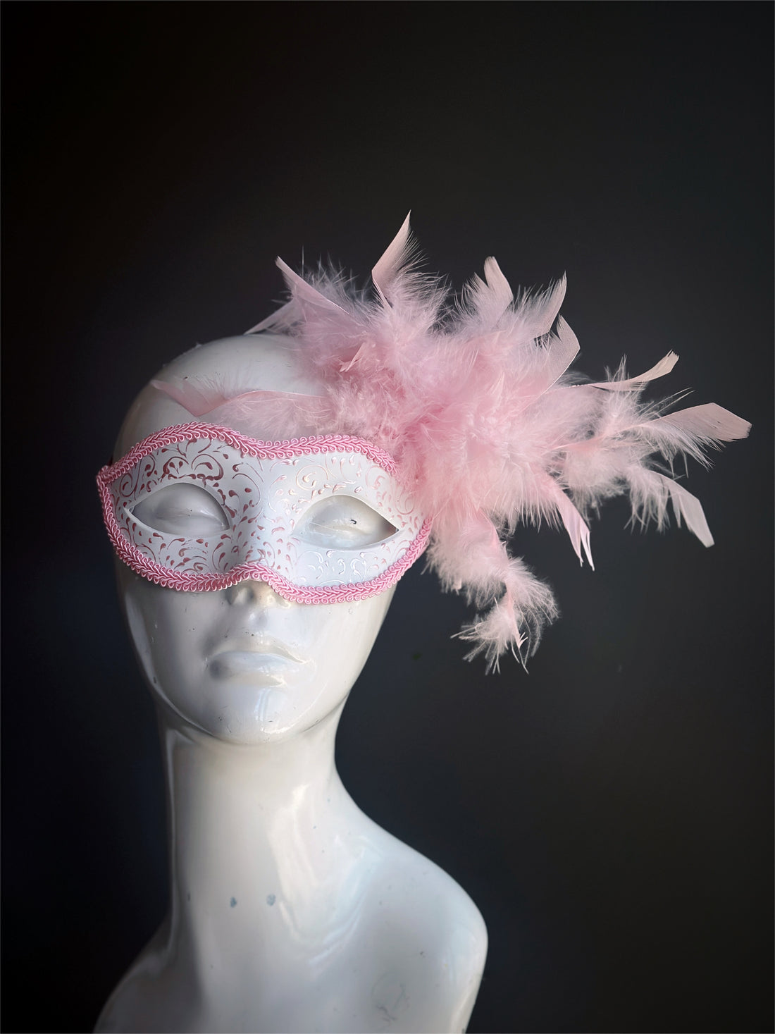 Elegant masquerade mask in pink and white with soft feathers and glittery accents, perfect for sweet and feminine party looks.