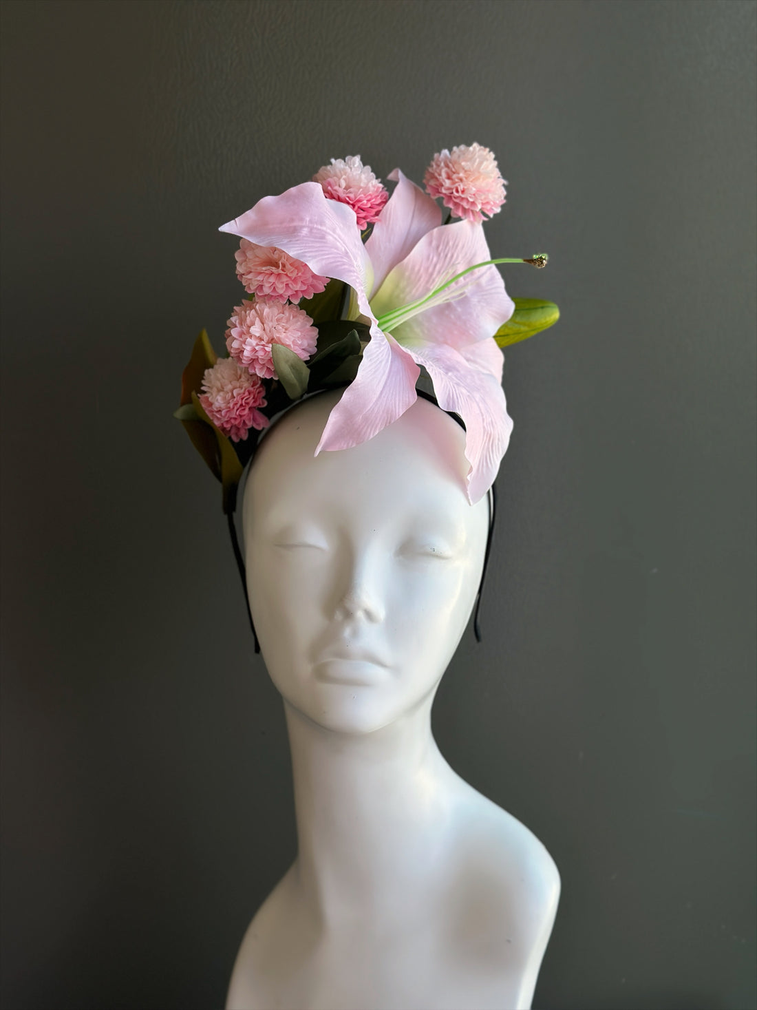 Pink lily fascinator hat with floral design for derby, weddings, and garden party events.