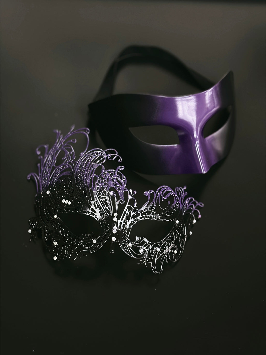Purple and black masquerade couples masks, one sleek and one ornate metal lace design with rhinestones, ideal for Venetian masquerade balls and parties.