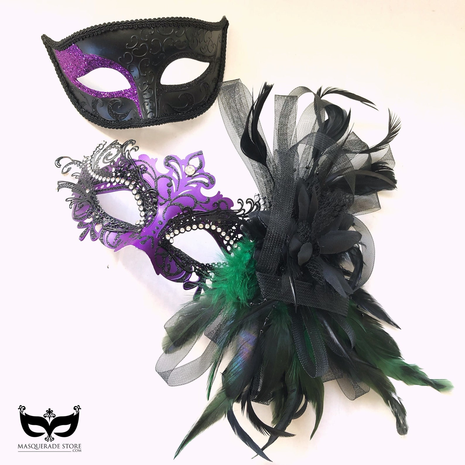 Couple’s masquerade mask set with a women’s purple rhinestone feather mask and a men’s black scrollwork mask with purple glitter.