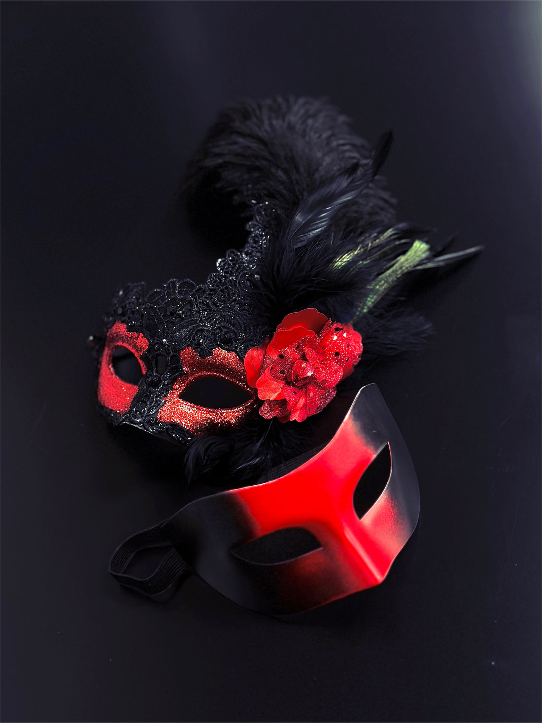 Red and black masquerade couples masks, one with lace, glitter, feathers, and a red floral accent, perfect for Venetian masquerade balls and Mardi Gras.