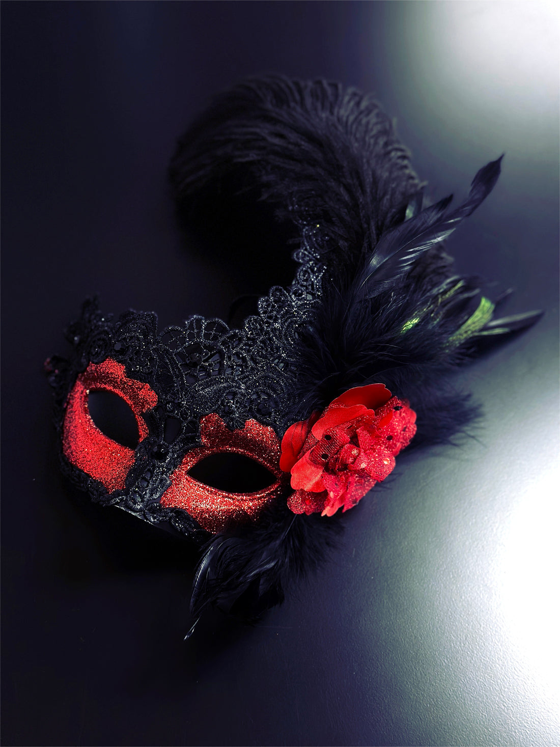 Red and black women’s masquerade mask with lace, glitter, feathers, and a red flower accent, designed for Venetian masquerade balls and Mardi Gras events.