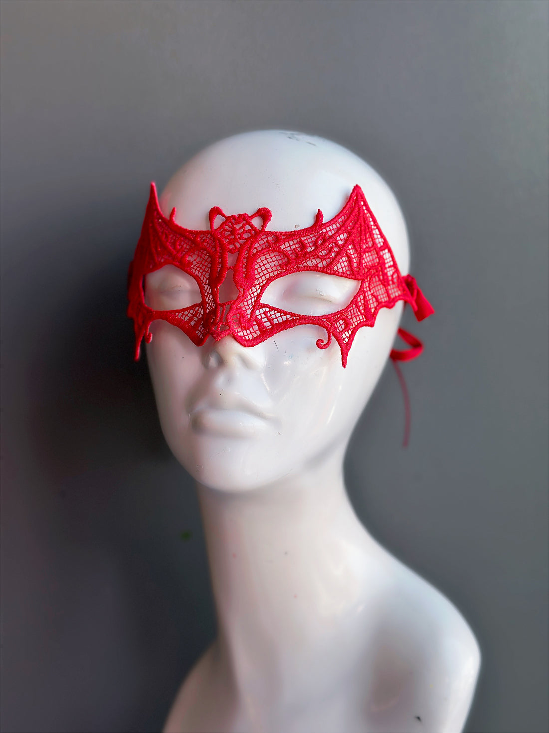 Red lace masquerade mask with bat wings and gothic cutout design.