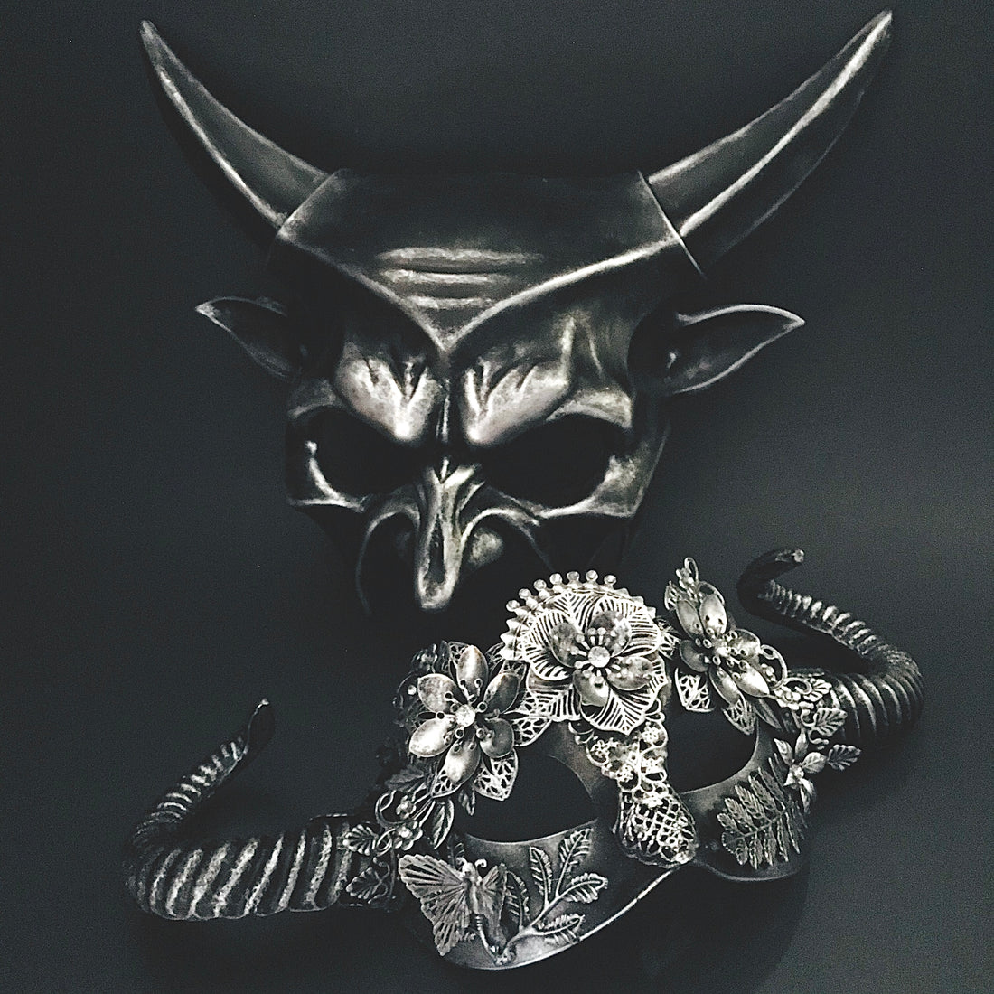 Gothic silver masquerade mask pair featuring sculpted horns, filigree flowers, and fantasy-inspired details.