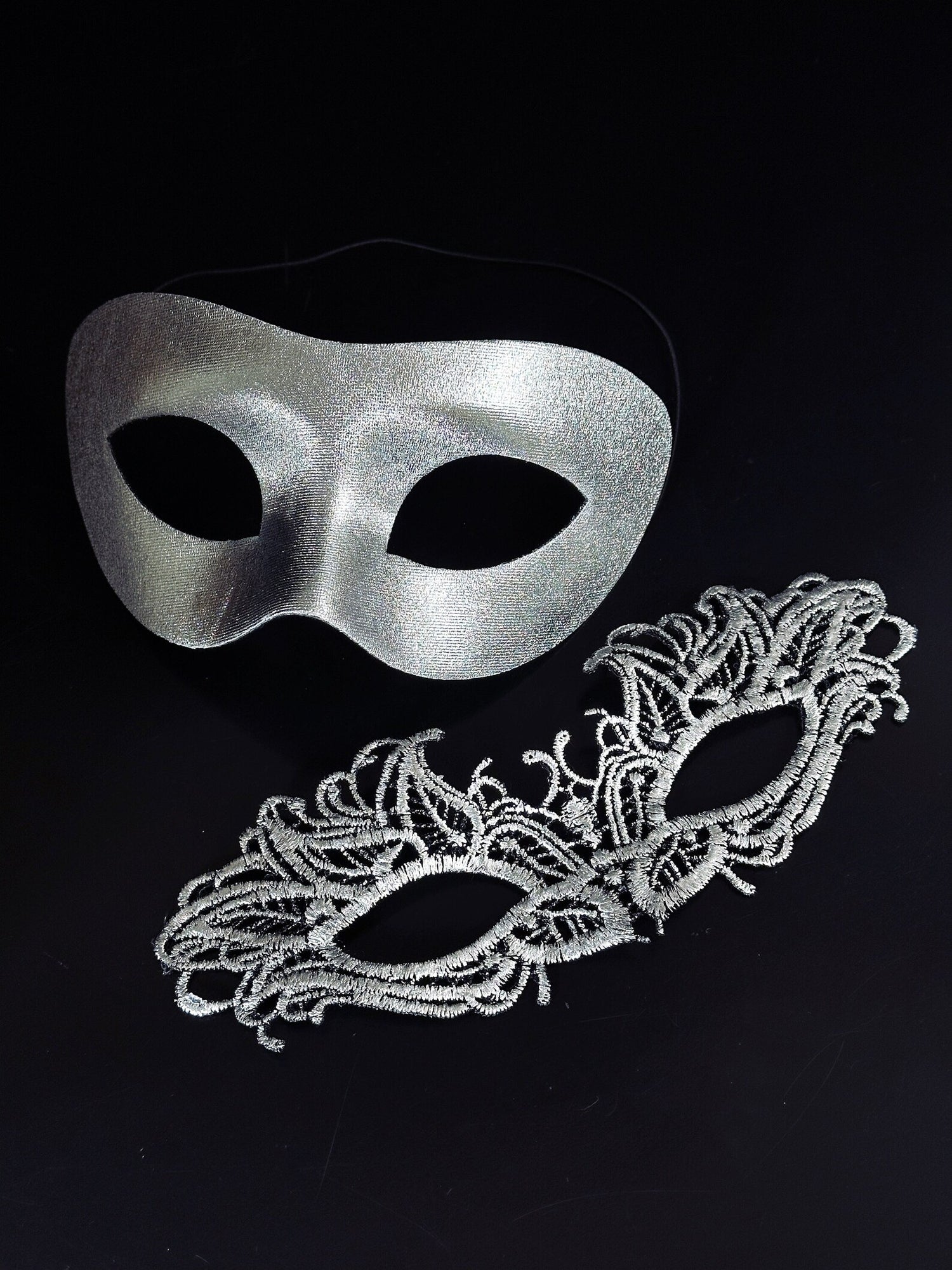 Silver metallic couples masquerade masks featuring a sleek men’s mask and a delicate lace women’s mask, ideal for Venetian balls, weddings, and formal celebrations.