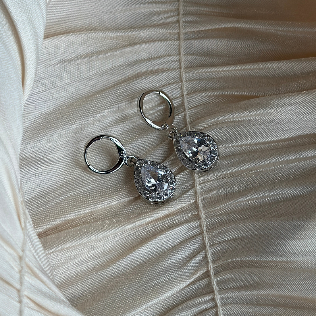 Pair of sparkling silver crystal earrings displayed on cream silk background